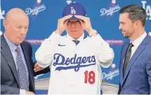  ?? Ashley Landis/Associated Press ?? Yoshinobu Yamamoto, center, puts on his new uniform next to president and CEO Stan Kasten, left, and Executive Vice President and General Manager Brandon Gomes during his introducti­on as a new member of the Los Angeles Dodgers Wednesday in Los Angeles.