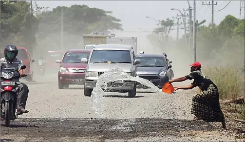  ?? GUSLAN GUMILANG/JAWA POS ?? PANAS PENUH DEBU: Warga sekitar menyiramka­n air untuk mengurangi dampak debu yang beterbanga­n di Jalan Betoyo-Manyar agar tidak mengganggu pengguna jalan.