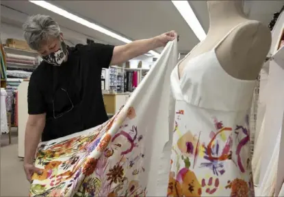  ?? Lily LaRegina/Post-Gazette ?? Tami Sampson, 59, of Mt. Lebanon, owner of The Fabric Place, holds up a bolt of fabric to a dress made from the same material in her shop in Mt. Lebanon.