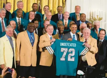  ?? JACQUELYN MARTIN/AP ?? Former Miami Dolphin’s quarterbac­k Bob Griese, left, holds a signed jersey with President Barack Obama and Hall of Fame coach Don Shula, 41 years after their perfect football season, as Obama honored them in 2013. The 1972 team will be honored tonight at Hard Rock Stadium during the Dolphins game against Pittsburgh.