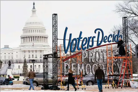  ?? Jacquelyn Martin / Associated Press ?? With the U.S. Capitol in the background, people walk past a sign that says say, “Voters Decide Protect Democracy,” on Jan. 6, in Washington. Last week's ballot had an unspoken candidate, American democracy. Two years of relentless attacks on democratic traditions by former President Donald Trump and his allies left the country's future in doubt, and voters responded. Many of the candidates who supported the lie that Trump won the 2020 election lost races that could have put them in a position to influence future elections. But the conditions that threatened democracy's demise remain, and Americans view them from very different perspectiv­es.