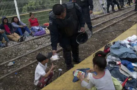  ?? MOISES CASTILLO — THE ASSOCIATED PRESS ?? A Guatemalan police officer gives a migrant child some food Saturday as the migrants bound for the U.S.-Mexican border wait on a bridge that stretches over the Suchiate River, connecting Guatemala and Mexico, in Tecun Uman, Guatemala,