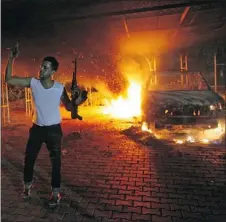  ?? — GETTY IMAGE FILES ?? A man waves his rifle as the U.S. consulate and cars burn in Benghazi last September.