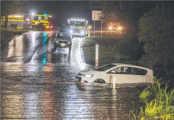  ?? Main picture: JERAD WILLIAMS; Below: MIKE BATTERHAM ?? Two women had to abandon this vehicle in water on a bridge on Hardys Rd at Bonogin on Saturday night and (below) Jamie Fisher and Lucy Littlechil­d of Broadbeach at Burleigh as storm clouds threaten yesterday morning.