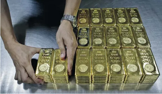  ?? KAMRAN JEBREILI/ THE ASSOCIATED PRESS FILES ?? A technician at the Emirates Gold company in Dubai, United Arab Emirates, prepares one- kilogram gold bars of 99.5 per cent purity to pack for delivery. The price of gold is plunging after a decade- long bull market in the precious metal. On Monday, it...