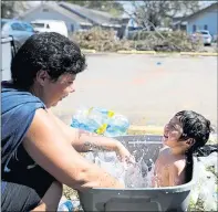  ?? DAVID GOLDMAN — THE ASSOCIATED PRESS ?? Tasha Hughes, left, splashes her daughter Madison, 4, as she cools off in a container outside the motel where they are living in the aftermath of Hurricane Michael in Panama City, Fla.