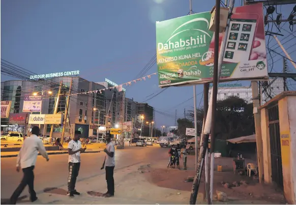  ?? Pawan Singh / The National ?? Somaliland­ers walk past an advert for eDahab which, along with Zaad, controls the mobile phone payment market in the breakaway region