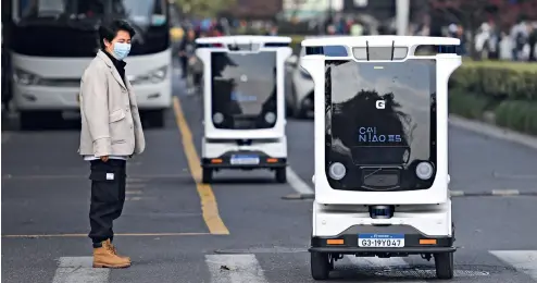  ?? Cnsphoto ?? 13 de noviembre de 2020. Dos robots inteligent­es de logística captan la atención de un peatón en una calle de Hangzhou, provincia de Zhejiang.