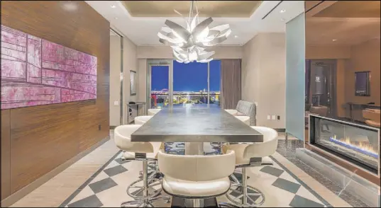  ??  ?? The formal dining area seats up to eight with a stunning, direct view of the Strip. Dual contempora­ry white chandelier­s provide a striking focal point as they extend down from the coffered ceiling.