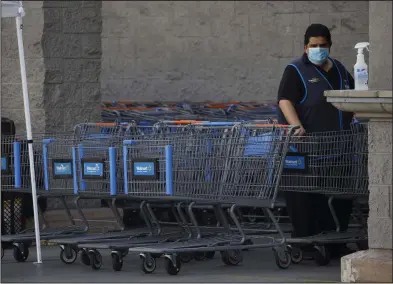  ?? Bloomberg News/Patrick T. Fallon ?? A Walmart employee cleans shopping carts to help prevent the spread of coronaviru­s at a Walmart Inc. store in Torrance, Calif., in May. Walmart only requires customers to wear masks in its stores where they are mandated by state or local ordinances.