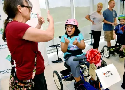  ?? Robin Rombach/Post-Gazette ?? Celebratin­g her birthday, Reese Randolph, 9, gives a thumbs up to her family friend Jackie Lignoski as she gets ready to ride the new bike she just received from the children's charity Variety as part of its “My Bike” program, which gives children with...