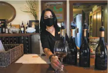  ??  ?? Michelle Taylor wears a mask as she serves guests at the reopened Papapietro Perry Winery in Healdsburg.