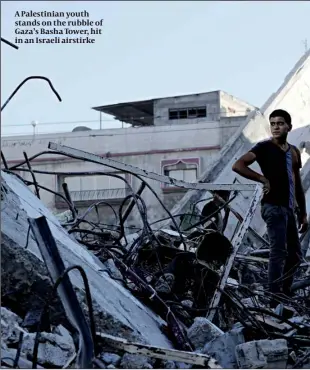  ??  ?? A Palestinia­n youth stands on the rubble of Gaza’s Basha Tower, hit in an Israeli airstirke