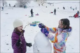  ?? SARAH A. MILLER — IDAHO STATESMAN VIA AP ?? Friends Addie Palmer, 7, left, and Esther Roghaar, 7, use tree branches to make arms and hair on their snowman at Camel’s Back Park in Boise, Idaho, on Monday.