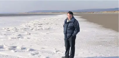  ?? Picture: Carmarthen Journal archives ?? The then chairman of Pendine Community Council, Simon Morris, surveys the unusual sight of an apparently frozen sea edge at Pendine Sands in January 2010.