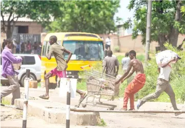  ?? — AFP photo ?? People run with loot from a local supermarke­t during at shutdown demonstrat­ion in Bulawayo after the president announced a more than hundred per cent hike in fuel prices.