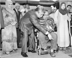  ??  ?? Zahid (centre) helping MohdYunus Jaafar into the new wheelchair at the 1Pesara Malaysia Assembly in Serdang. - Bernama photo