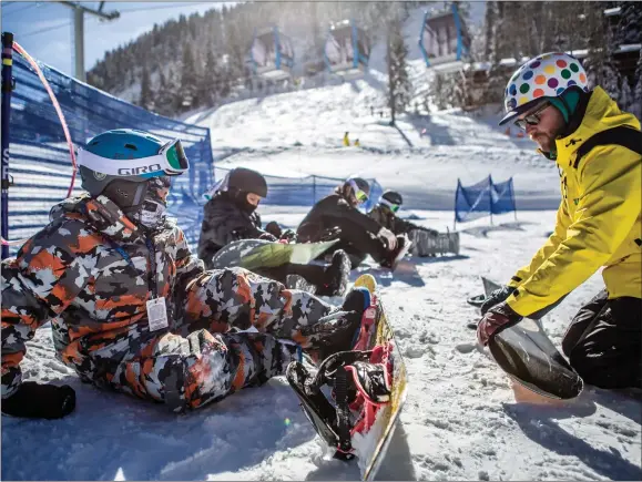  ?? NATHAN BURTON/Taos News ?? Geronimo Pino, left, straps up during a snowboard lesson Sunday (Jan. 22) at Taos Ski Valley.