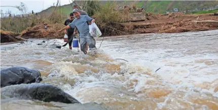  ?? GERALD HERBERT, AP ?? Men make their way across the Rio San Lorenzo de Morovis after the bridge was swept away by Hurricane Maria.