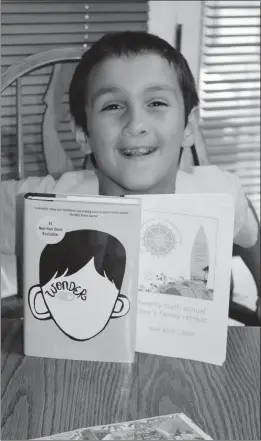  ??  ?? Kyle Atfimos, 8, smiles with “Wonder,” a book that is now being made into a movie. The book helped him realize his difference­s — being born with a cleft lip and palate — did not warrant bullying. His mother, Michelle, hopes local schools will...