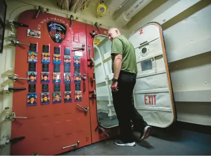  ?? ?? Sam Erwin, a New York City firefighte­r and military veteran, passes a display of photos of some of the firefighte­rs killed at the World Trade Center hanging in a passageway on the USS New York. Erwin was touring the amphibious transport dock ship Sunday at Naval Station Norfolk.