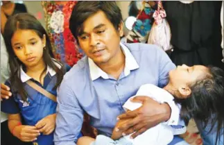  ?? PHA LINA ?? Meach Vireak, whose wife, Sok Vanna, was crushed by a timber-laden truck bearing military number plates, is photograph­ed with his two daughters at his residence yesterday.