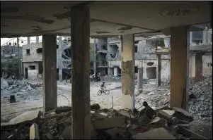  ??  ?? A boy rides his bike June 13 along Al-Baali Street next to houses heavily damaged by airstrikes during the 11-day war.