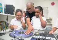  ??  ?? DJ Denvo introduces seven-year-old Lea Castera (left) and seven-year-old Elise McLaughlin of Reach Academy to the turntables during the weekly Kids Mix DJ Club.