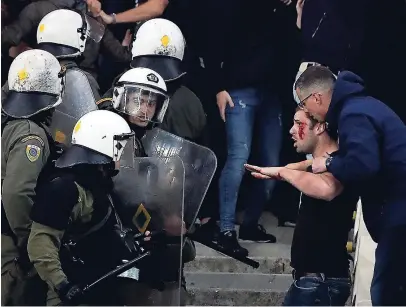  ?? AP ?? An Ajax fan holds another fan bleeding after riot police started beating Ajax fans after clashes broke out before the start of a Group E Champions League match between AEK Athens and Ajax at the Olympic Stadium in Athens on Tuesday.