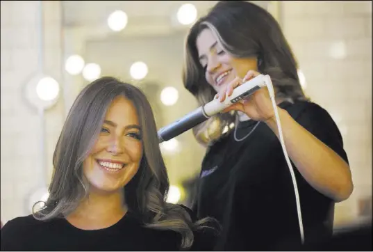  ?? Mark Lennihan The Associated Press ?? Hair salon owner Erika Wasser, left, has her hair touched up by stylist Samantha Sheppard at a Glam+Go studio in New York.
