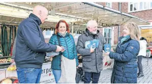  ?? FOTO: RUTH KLAPPROTH ?? Ralf Sester (2.v.r.) und Carsten Forg (l.) verteilen die Parkscheib­en auf dem Markt in Hückelhove­n.