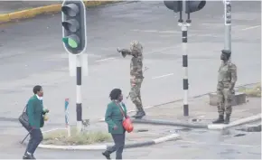  ??  ?? Armed soldiers stand on the road leading to President Robert Mugabe’s office, as school children.