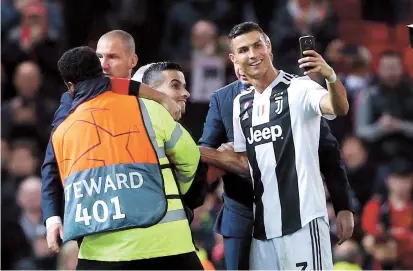  ??  ?? Juventus’ Cristiano Ronaldo takes a selfie with a pitch invader as stewards apprehend the fan following the UEFA Champions League Group H match against Manchester United at Old Trafford in Manchester on Tuesday. Right: United manager Jose Mourinho is seen before the match, which his team lost 0-1. — Reuters