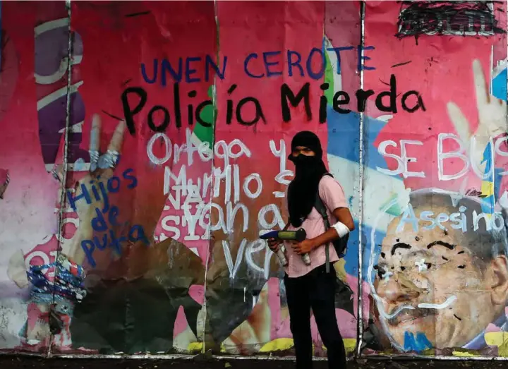  ??  ?? DEMONSTRAN­T: Denne demonstran­ten poserer foran et vandaliser­t bilde av president Daniel Ortega og visepresid­ent Rosario Murillo i Managua.