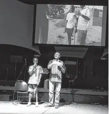  ??  ?? Fidele appears on stage with Mike Cousineau, founder of nonprofit humanitari­an organizati­on 1040i, speaking in Norman.