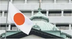  ??  ?? A Japanese flag flutters atop the Bank of Japan building in Tokyo. Japan posted its third consecutiv­e trade surplus yesterday as November exports held up, boosted by a sharp slide in the yen. — Reuters photo