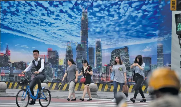  ?? Photo: AFP ?? People crossing a road in front of a billboard on the wall of a constructi­on site in Beijing’s central business district.