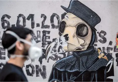  ??  ?? Street artist Angel Crow wearing a protective mask stands next to one of his artworks on a wall during a lockdown in Paris that aimed at curbing the spread of the COVID-19 disease. — AFP