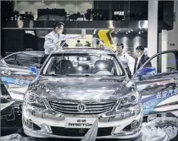  ?? BLOOMBERG ?? A self-driving car manufactur­ed by Chongqing Changan Automobile Co, a modified version of its Raeton sedan, stands on display as a technician fixes a sensor onto its roof at the Beijing Internatio­nal Automotive Exhibition in Beijing in April.