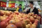  ?? THE ASSOCIATED PRESS ?? A woman wearing a uniform with the logo of an American produce company helps a customer shop for apples a supermarke­t in Beijing on Friday.