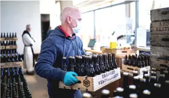  ?? Photos ?? An employee wearing a protective facemask and gloves carry a crates full of Westvleter­en beer at the shop of the SaintSixtu­s abbey, in Westvleter­en as the trappist monks resume to sell their beer, with new social distancing measures, while the country eases lockdown measures taken to curb the spread of the Covid-19 (the novel coronaviru­s).