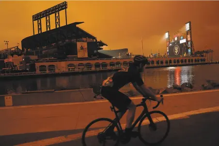  ?? Scott Strazzante / The Chronicle ?? A cyclist rides near McCovey Cove as an orange haze hangs over Oracle Park before a MarinersGi­ants game on Sept. 9.