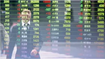  ?? — Reuters ?? A man is mirrored in front of an electronic board showing stock informatio­n at a brokerage firm in Tokyo.