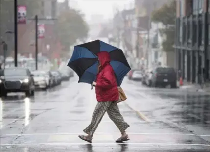  ?? DARREN CALABRESE, THE CANADIAN PRESS ?? A woman shields herself from the rain while walking in downtown in Halifax. High winds moved from Quebec to Atlantic Canada Monday.