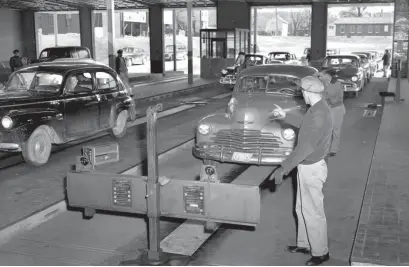  ?? THE COMMERCIAL APPEAL ?? Both aim and focus are checked on headlights using a crossboard containing light-sensitive instrument­s by Mr. Lee at the City of Memphis vehicle testing station on Washington Avenue on March 2, 1952. The driver, still in the car, is told to switch from bright lights to dim to ascertain if the beams are at proper angle and not blinding.