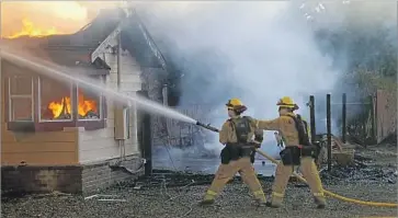  ?? Adam L. Wiedmann European Pressphoto Agency ?? FIREFIGHTE­RS try to suppress the flames at a home as the Clayton fire overtakes Lower Lake. After the fire erupted, thousands of people were evacuated from Lake County, where 24% of residents live in poverty.