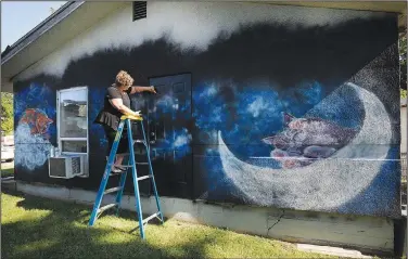  ?? NWA Democrat-Gazette/ANDY SHUPE ?? Shelby Nichols of Rogers paints a fish July 26 on the south wall of the Outback Cat House Rescue in Rogers. Rogers Experiment­al House donated the paint for the project, and Nichols donated her time. A fundraiser is set up on Facebook to raise money for Nichols and the cat house.