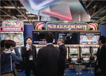  ?? PHILIPPE LOPEZ/AFP ?? An exhibitor from Japan talks to visitors in front of slot machines at the Global Gaming Expo Asia in the world’s biggest gambling hub of Macau in May 2015.