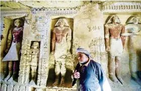  ?? AFP ?? An Egyptian archaeolog­ical laborer is seen walking near statues in a newly discovered tomb at Saqqara necropolis, on Saturday.