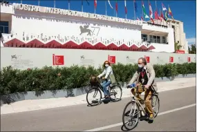  ?? PHOTO BY JOEL C. RYAN/INVISION/AP ?? Festival attendees cycle in front of the main cinema ahead of the start of the 77th edition of the Venice Film Festival in Venice, Italy, Tuesday, Sept. 1, 2020. Italy was among the countries hardest hit by the coronaviru­s pandemic, and the festival will serve as a celebratio­n of its re-opening and a sign that the film world, largely on pause since March, is coming back as well.